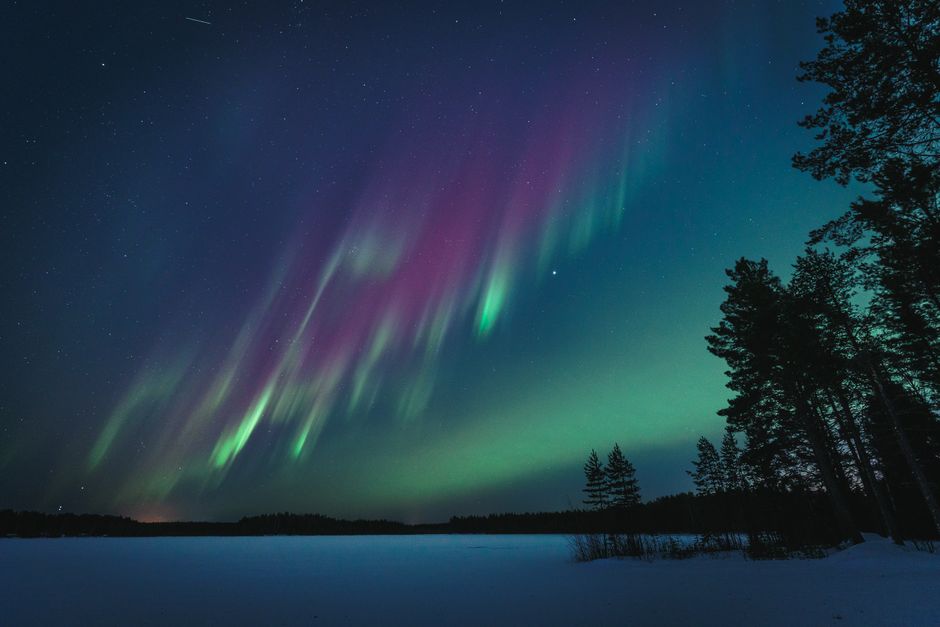 Northern lights illuminate the night sky over a serene lake in Oulu, Finland